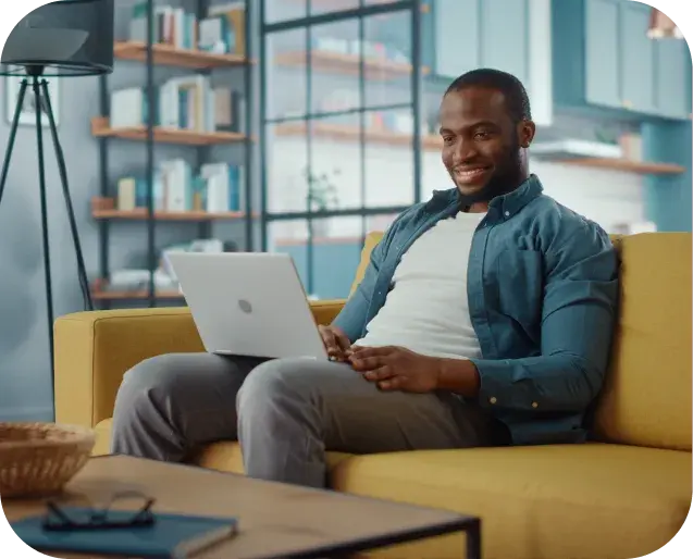 Man using a laptop while seated on a couch, representing employee benefits administration and account management.