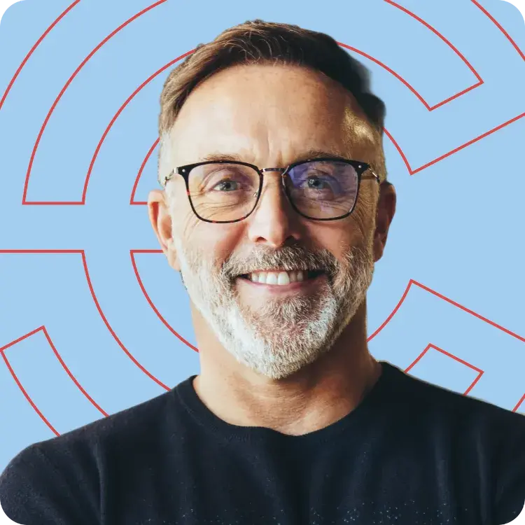 Smiling man with glasses wearing a dark sweater against a light blue background.